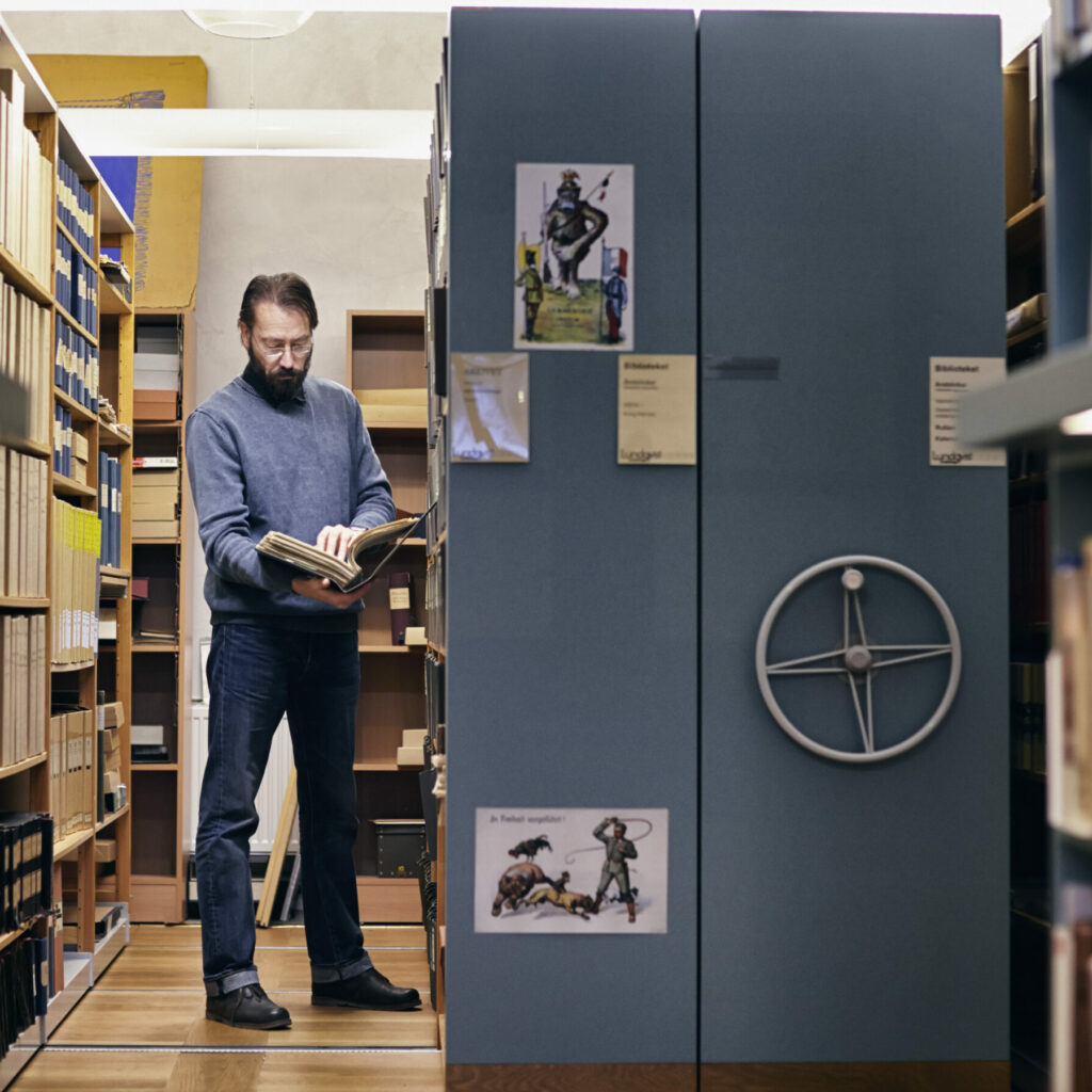 En man står vid en av arkivets många rullhyllor och läser i en pärm. 