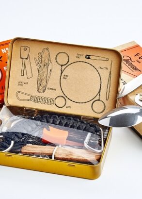 Ett &ouml;verlevnadskit i orange pl&aring;task best&aring;ende av f&auml;llkniv, t&auml;ndst&aring;l, rep, tr&aring;ds&aring;g, pincett och s&auml;kerhetsn&aring;lar.