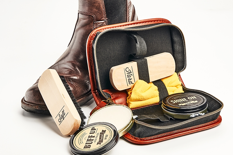 Ett skoputsningskit med borstar, putsduk och vax i ett skinnetui st&aring;r lutat mot en brun k&auml;nga.