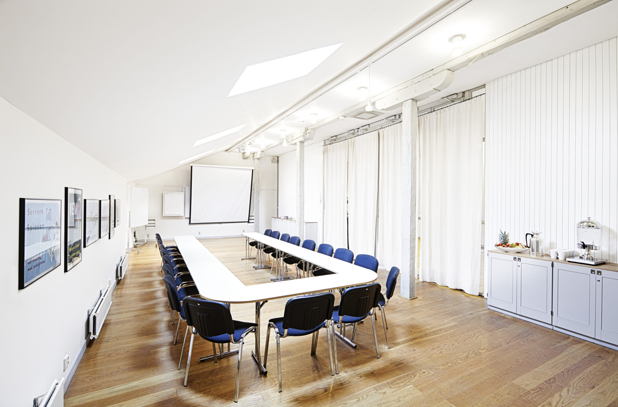 Ett konferensrum med bord och stolar formade i en b&aring;ge riktad mot en sk&auml;rm