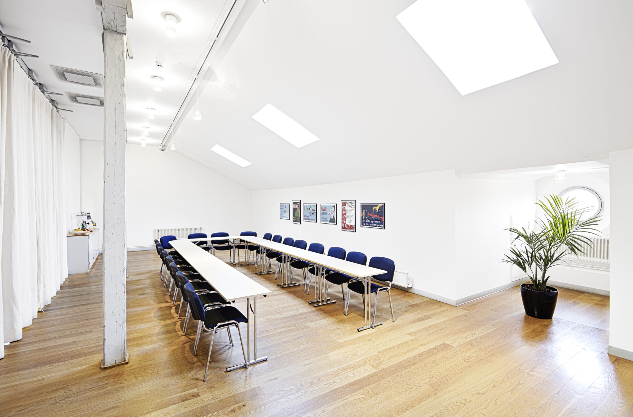 Ett vitt luftigt rum med takf&ouml;nster, utrustat med ett u-format bord med m&aring;nga stolar.