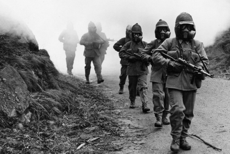 Soldater g&aring;r p&aring; led med vapen i famnen och gasmask &ouml;ver ansiktena.