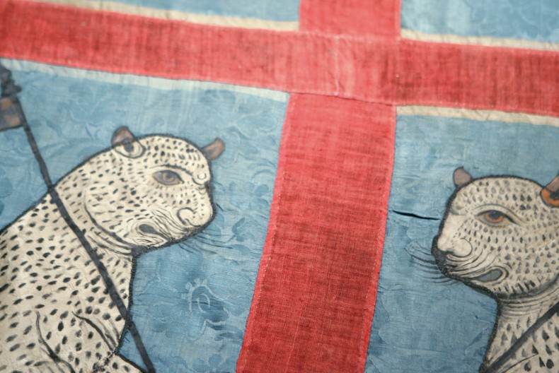 En n&auml;rbild p&aring; en fana med r&ouml;tt kors mot bl&aring; botten och tv&aring; kattdjur v&auml;nda mot varandra