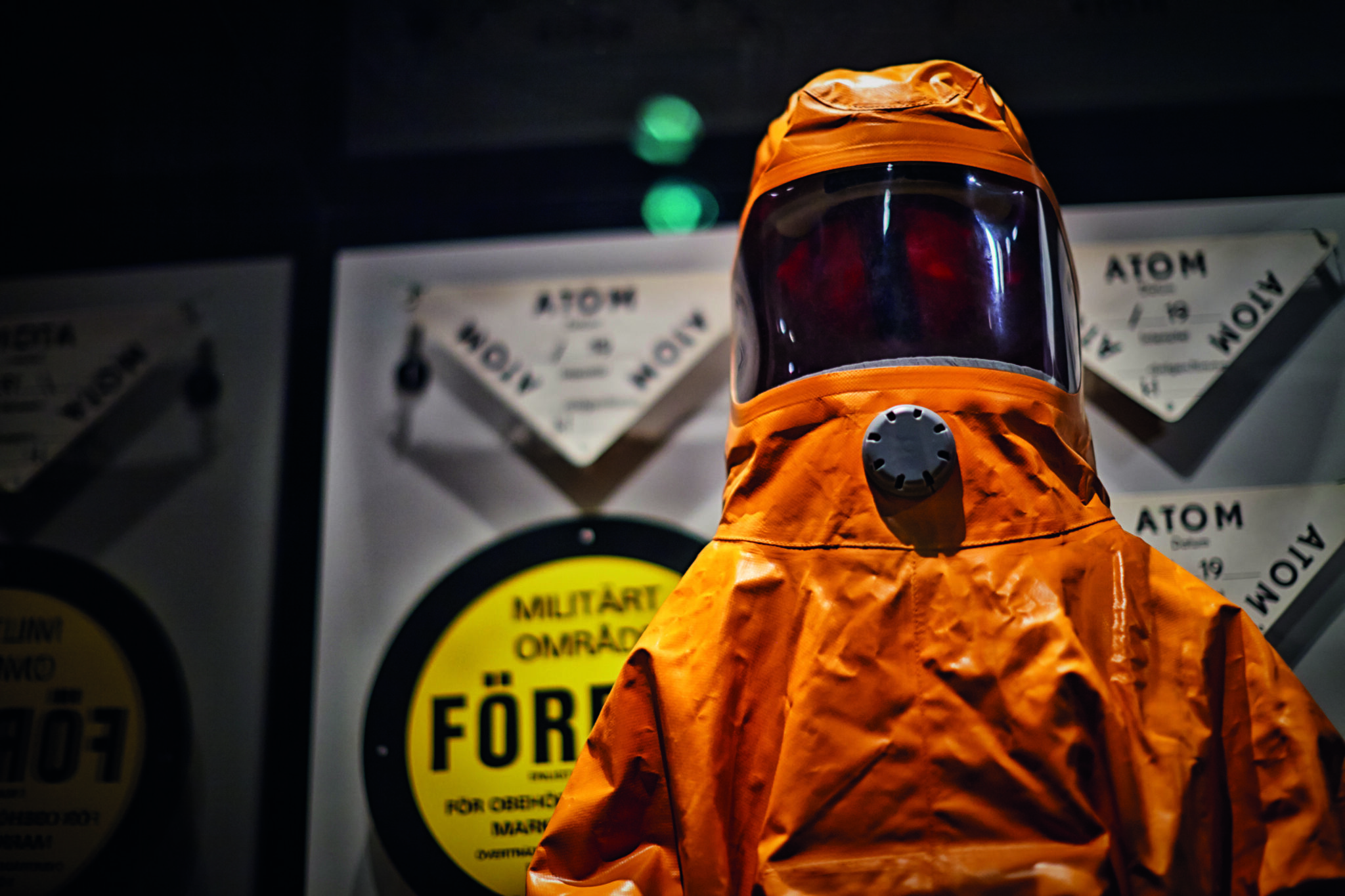En helkroppst&auml;ckande orange skyddsdr&auml;kt framf&ouml;r uppsatta varningsskyltar som det bland annat st&aring;r "Atom" och "Milit&auml;rt omr&aring;de" p&aring;.