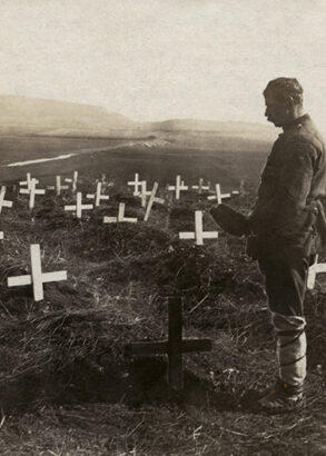 En man med m&ouml;ssan i hand st&aring;r vid ett av m&aring;nga kors nedstuckna i jorden p&aring; en stor &auml;ng.