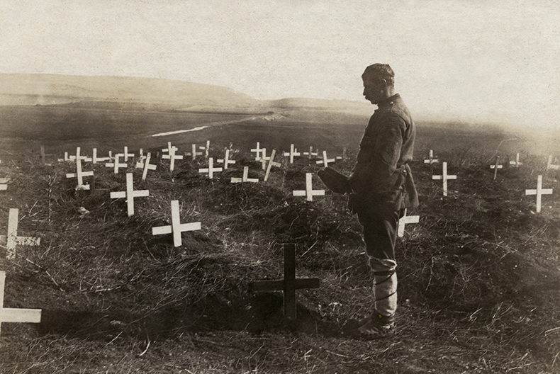 En man med m&ouml;ssan i hand st&aring;r vid ett av m&aring;nga kors nedstuckna i jorden p&aring; en stor &auml;ng.