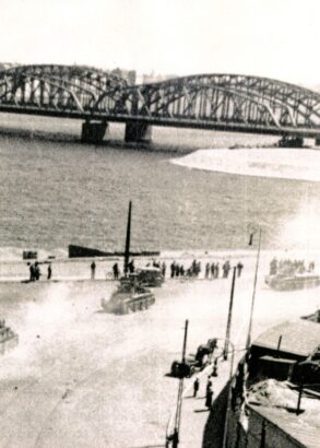 Milit&auml;rfordon k&ouml;r l&auml;ngs vatten. L&auml;ngre bort syns en l&aring;ng bro.