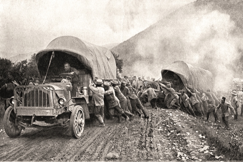 Svartvit bild av en stor folkmassa som hj&auml;lper tv&aring; lastbilar upp p&aring; v&auml;gen igen. V&auml;gen &auml;r lerig och den ena lastbilen verkar ha problem att komma upp ur ett dike.