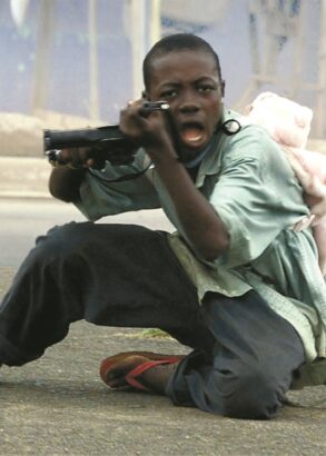 Ett barn med en ryggs&auml;ck i form av en nalle p&aring; ryggen riktar ett vapen mot den som tog bilden.