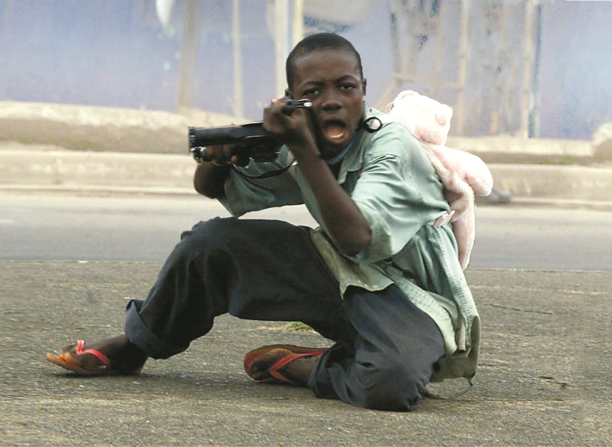 Ett barn med en ryggs&auml;ck i form av en nalle p&aring; ryggen riktar ett vapen mot den som tog bilden.