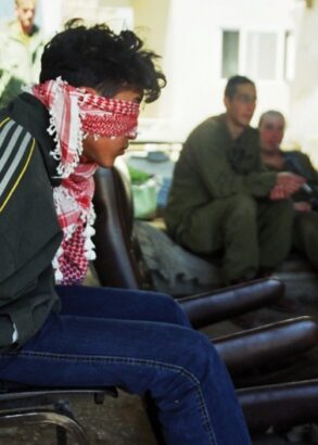 I f&ouml;rgrunden en bakbunden man p&aring; en stol och med f&ouml;rbundna &ouml;gon. I bakgrunden tre gr&ouml;nkl&auml;dda m&auml;n som ser ut att v&auml;nta p&aring; n&aring;got.