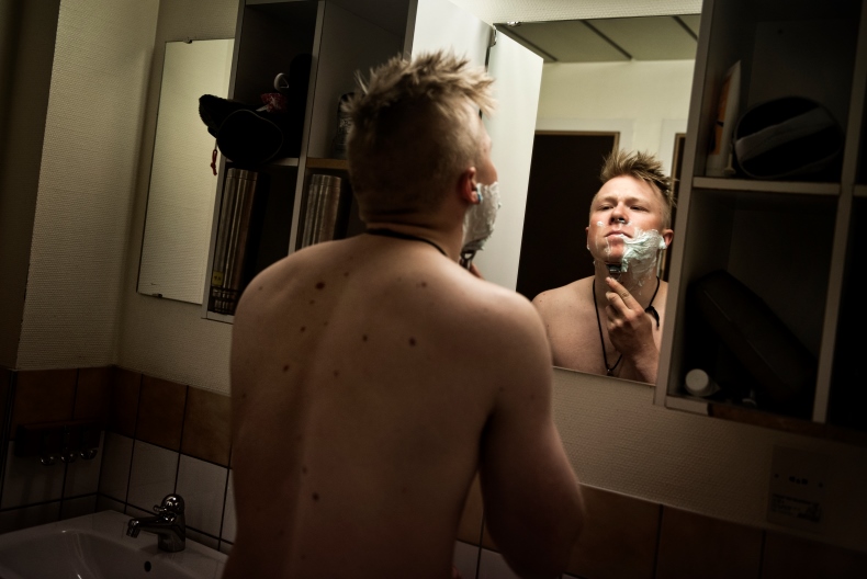 En person st&aring;r framf&ouml;r en spegel och rakar sig i ett badrum.