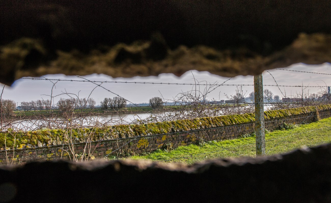 Som att titta ut ur ett g&ouml;mst&auml;lle och se en l&aring;ng &ouml;verv&auml;xt mur med taggtr&aring;d p&aring; som f&ouml;ljer vattnet. P&aring; andra sidan vattnet skymtas tr&auml;d och gr&ouml;nomr&aring;den.