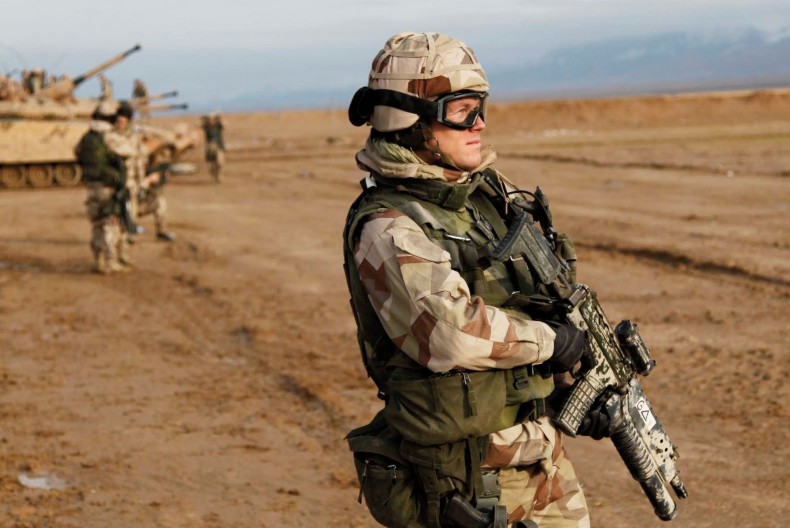 En soldat i full mundering och ett stort vapen i h&auml;nderna st&aring;r och blickar mot horisonten. Snett bakom soldaten st&aring;r en stridsvagn och fler soldater.