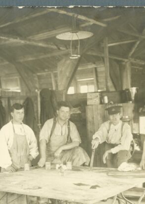 Fem vitkl&auml;dda sjukv&aring;rdare if&ouml;rda f&ouml;rkl&auml;den st&aring;r vid ett vitt bord i en timrad byggnad.