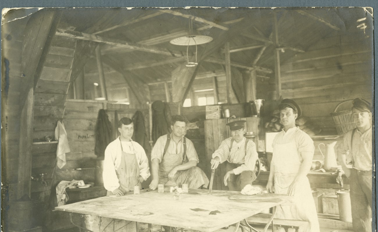 Fem vitkl&auml;dda sjukv&aring;rdare if&ouml;rda f&ouml;rkl&auml;den st&aring;r vid ett vitt bord i en timrad byggnad.