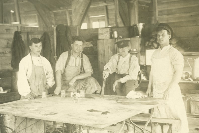 Fem vitkl&auml;dda sjukv&aring;rdare if&ouml;rda f&ouml;rkl&auml;den st&aring;r vid ett vitt bord i en timrad byggnad.