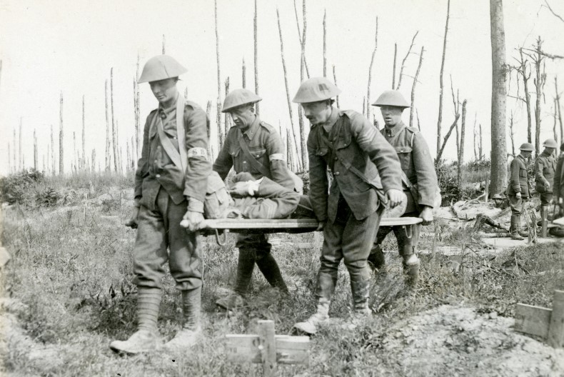 Fyra personer if&ouml;rda uniform och hj&auml;lm b&auml;r p&aring; en person liggandes p&aring; en b&aring;r