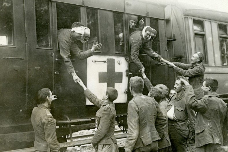 Skadade soldater h&auml;nger ut genom f&ouml;nstret p&aring; ett t&aring;g och tar farv&auml;l av sina kamrater st&aring;endes p&aring; perrongen. T&aring;get &auml;r m&auml;rkt med sjukv&aring;rdens kors.