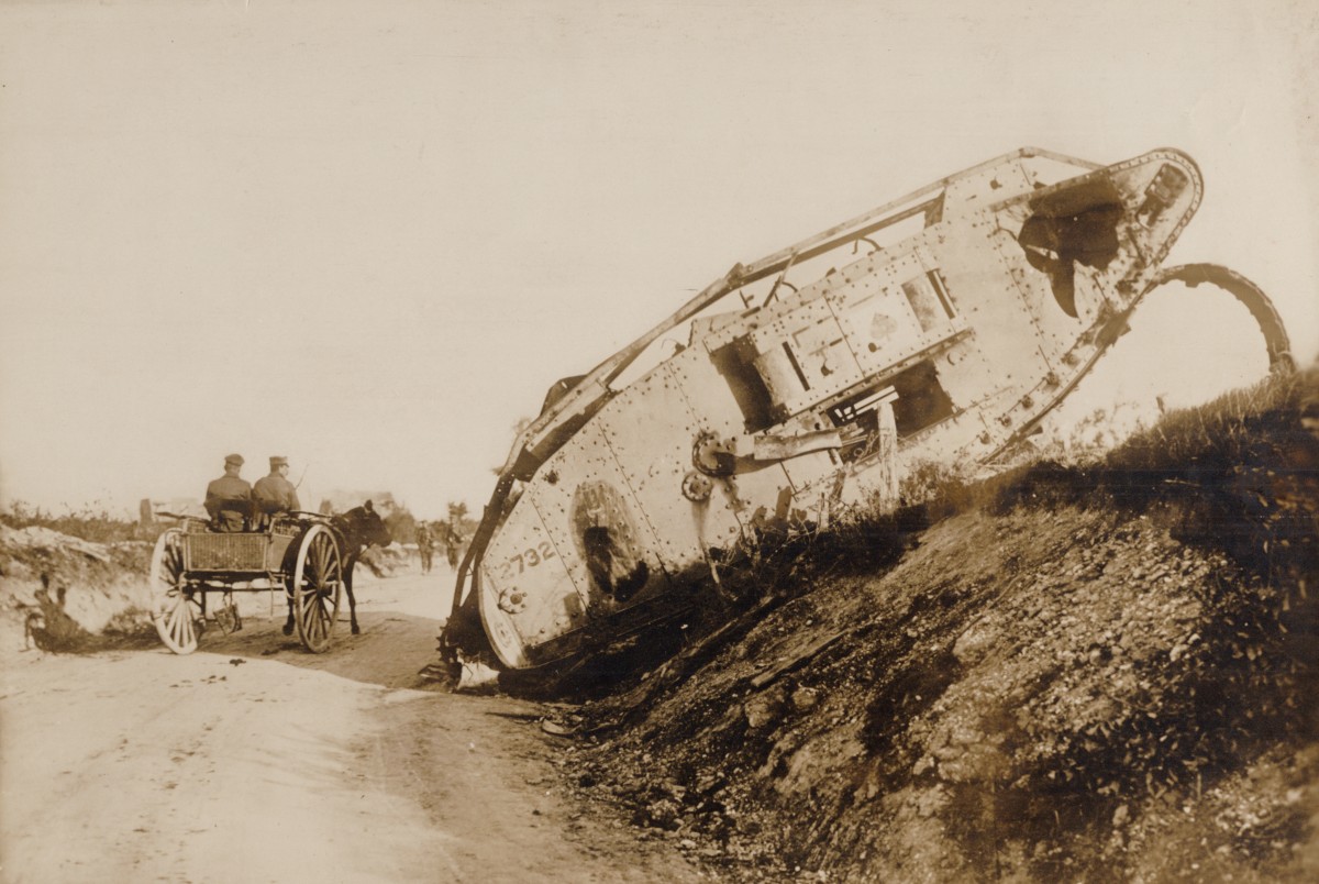 En stridsvagn har fastnat i terr&auml;ngen, en h&auml;st med vagn med tv&aring; passagerare passerar den p&aring; v&auml;gen bredvid.