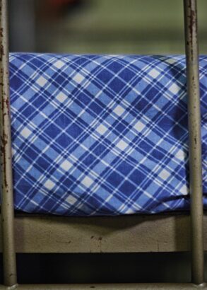 Del av en v&aring;ningss&auml;ng i j&auml;rn fr&aring;n lumpen, med bl&aring;vitrutiga, v&auml;lstr&auml;ckta lakan.