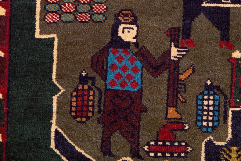 En del av en v&auml;vd matta som visar en f&auml;rggrann figur, en stridsvagn och handgranater.