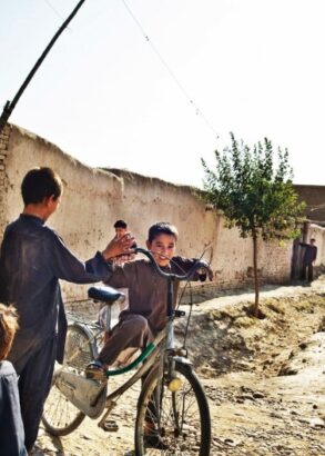 N&aring;gra barn leker l&auml;ngs en stenmur, en cyklar p&aring; en f&ouml;r stor cykel. Tv&aring; soldater ser ut att patrullera genom omr&aring;det.
