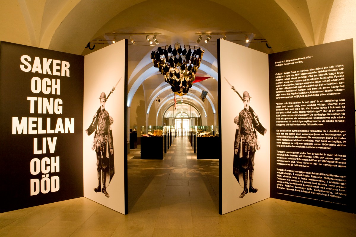 "Saker och ting mellan liv och d&ouml;d" st&aring;r vid entr&eacute;n till en utst&auml;llning. Innanf&ouml;r de &ouml;ppna d&ouml;rrarna som pryds av en varsin soldatillustration skymtas glasmontrar med utst&auml;llningsf&ouml;rem&aring;l.