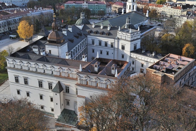 En bild ovanifr&aring;n &ouml;ver ett vitt slott med svart tak, tinnar och torn, slottet i Vilnius. Runtom &auml;r det lummigtl&auml;ngre bort syns andra byggnader.