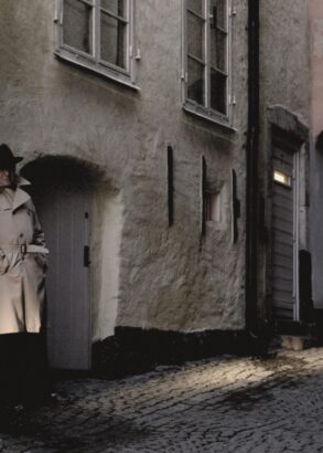 Tv&aring; personer i en m&ouml;rk gr&auml;nd. Ikl&auml;dda trenchcoats och hattar.