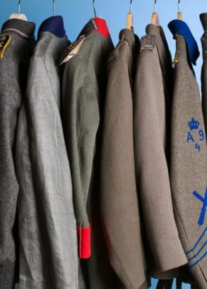 Nio uniformsjackor h&auml;nger p&aring; galgar p&aring; rad. Sm&aring; detaljer skiljer dem &aring;t s&aring;som olika gr&aring; nyanser, ett r&ouml;tt slag, bl&aring; rev&auml;rer.