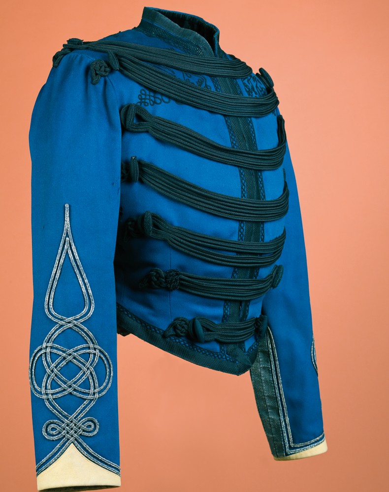 En klarbl&aring; uniformsliknande jacka med gr&ouml;na detaljer p&aring; br&ouml;stet och ett triballiknande broderi i gult p&aring; &auml;rmen.