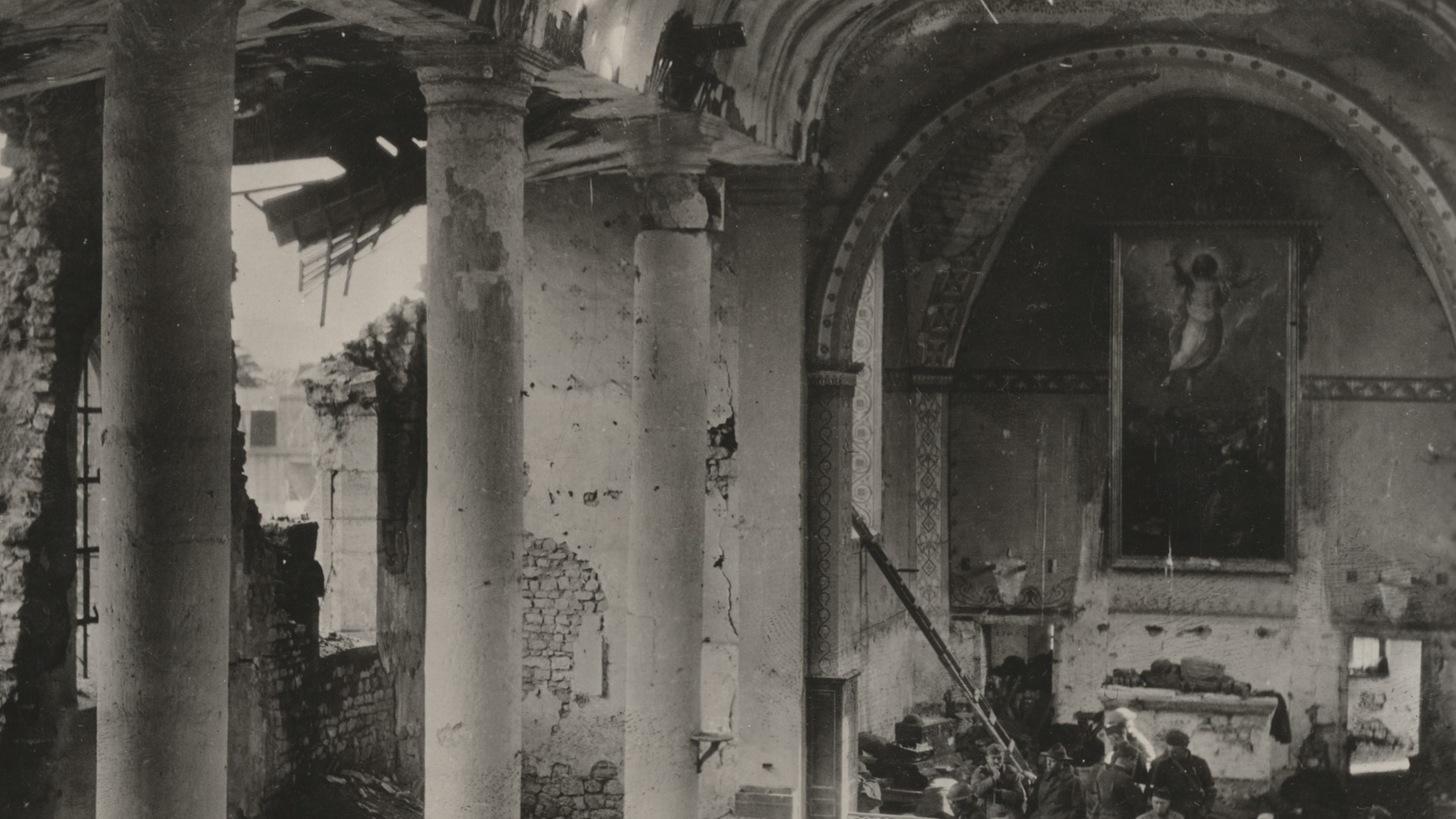 En pampig byggnad med pelare och valv har sargats av bomber. Det var troligtvis en kyrka d&aring; det h&auml;nger en stor tavla med religi&ouml;st motiv p&aring; en v&auml;gg.