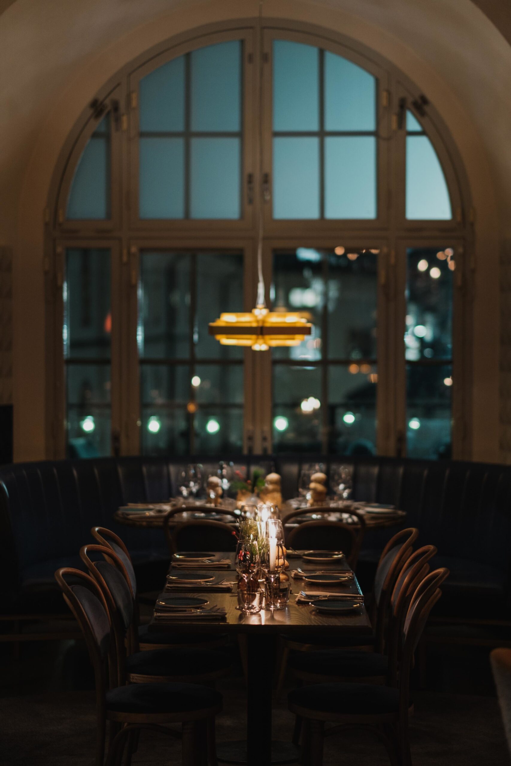 Ett dukat bord med st&auml;mningsfullt d&auml;mpat ljus och ett stort valvf&ouml;nster i bakgrunden.